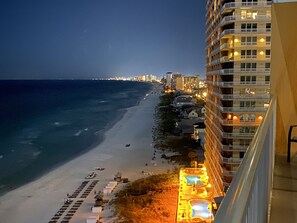 A beachfront hotel with a pool area, beach chairs, and a view of the ocean.