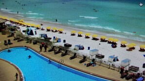A beach with a pool, sun loungers, umbrellas, and a lifeguard tower. - Updated Butler's Treasure Island,new master bath! Beach Service for 2 Included! (Panama  City  Beach)