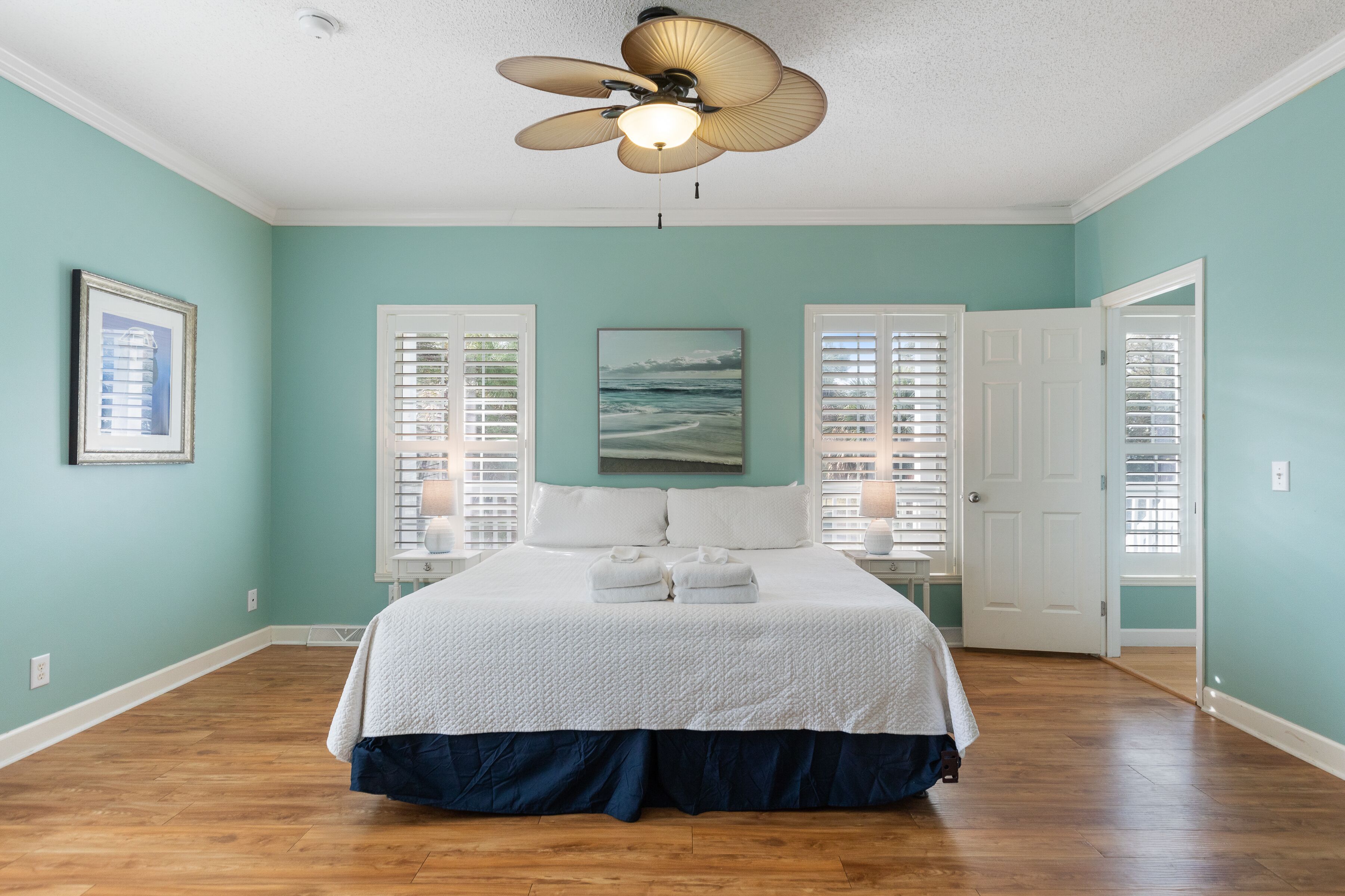 A bedroom with a bed, a ceiling fan, and a view of the ocean through the window.