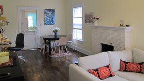 Un salon avec un canapé blanc, une cheminée, un coin repas avec des chaises et une table, et des œuvres d’art accrochées aux murs.