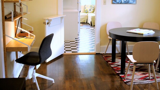 Un espace de vie compact comprenant un coin cuisine, un coin repas avec deux chaises, un sol à carreaux et un tableau accroché au mur.