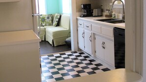 Une cuisine de taille réduite avec des meubles blancs, un carrelage noir et blanc, un réfrigérateur, un évier et une fenêtre qui laisse entrer la lumière naturelle.