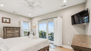 Ein Schlafzimmer mit Bett, Kommode, Fernseher und einem Balkon mit Aussicht.