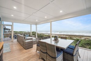 A covered outdoor area with wicker furniture and a table, overlooking the ocean. - BeachZilla! Oceanfront Pet Friendly! Screen Porch with Dining Area (Folly Beach)