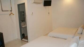 A hotel room with two beds, a TV mounted on the wall, and a bathroom with a sink and mirror.