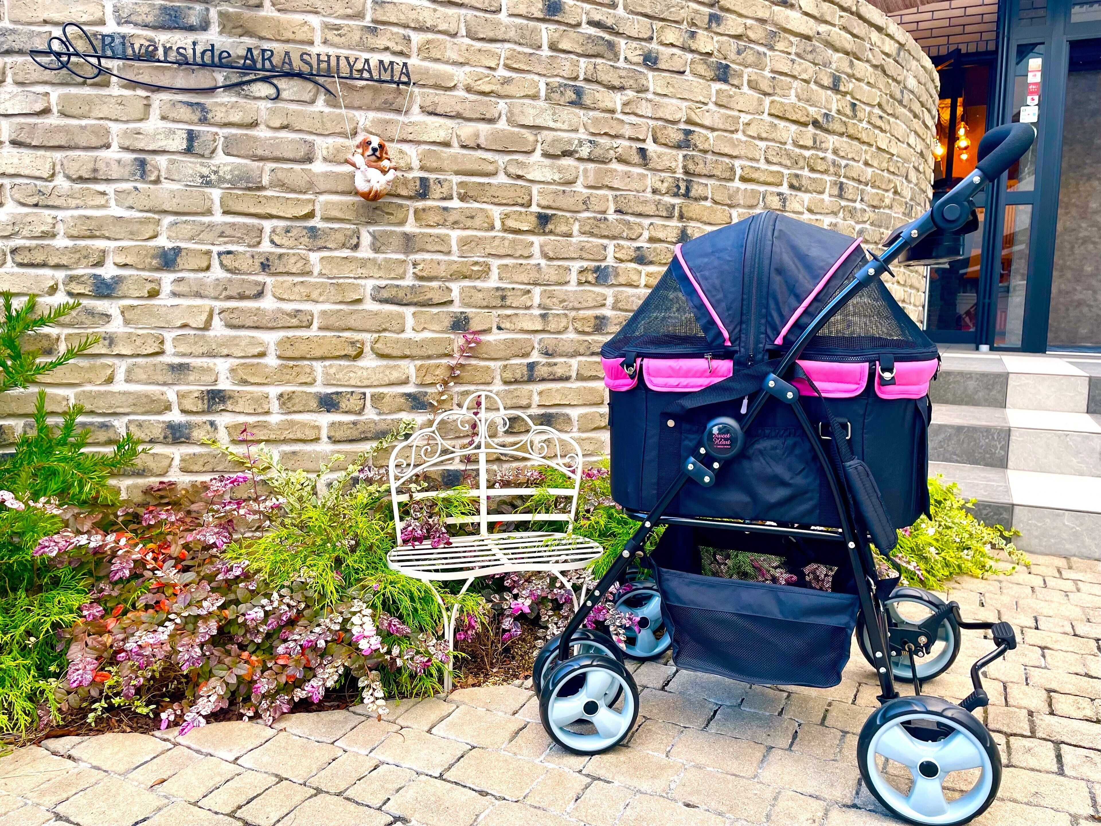A stroller with a black and pink design, a brick wall, and a sign that reads "Riverside ARA SHIYAMA".