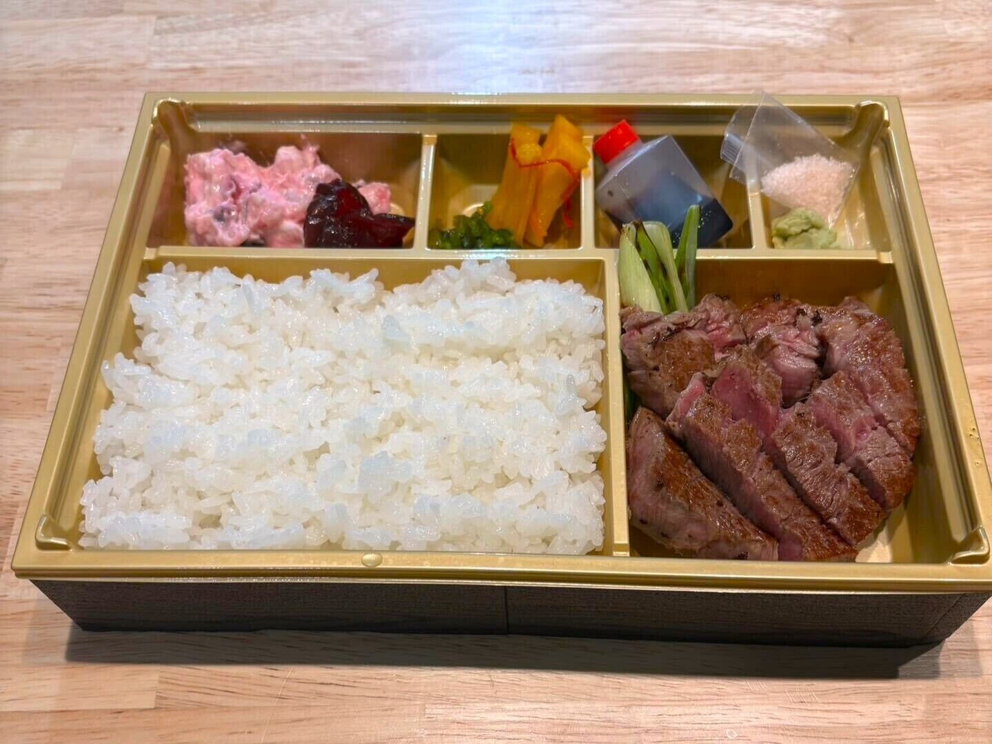 A bento box with white rice, sliced meat, pickled vegetables, and a small container of sauce.
