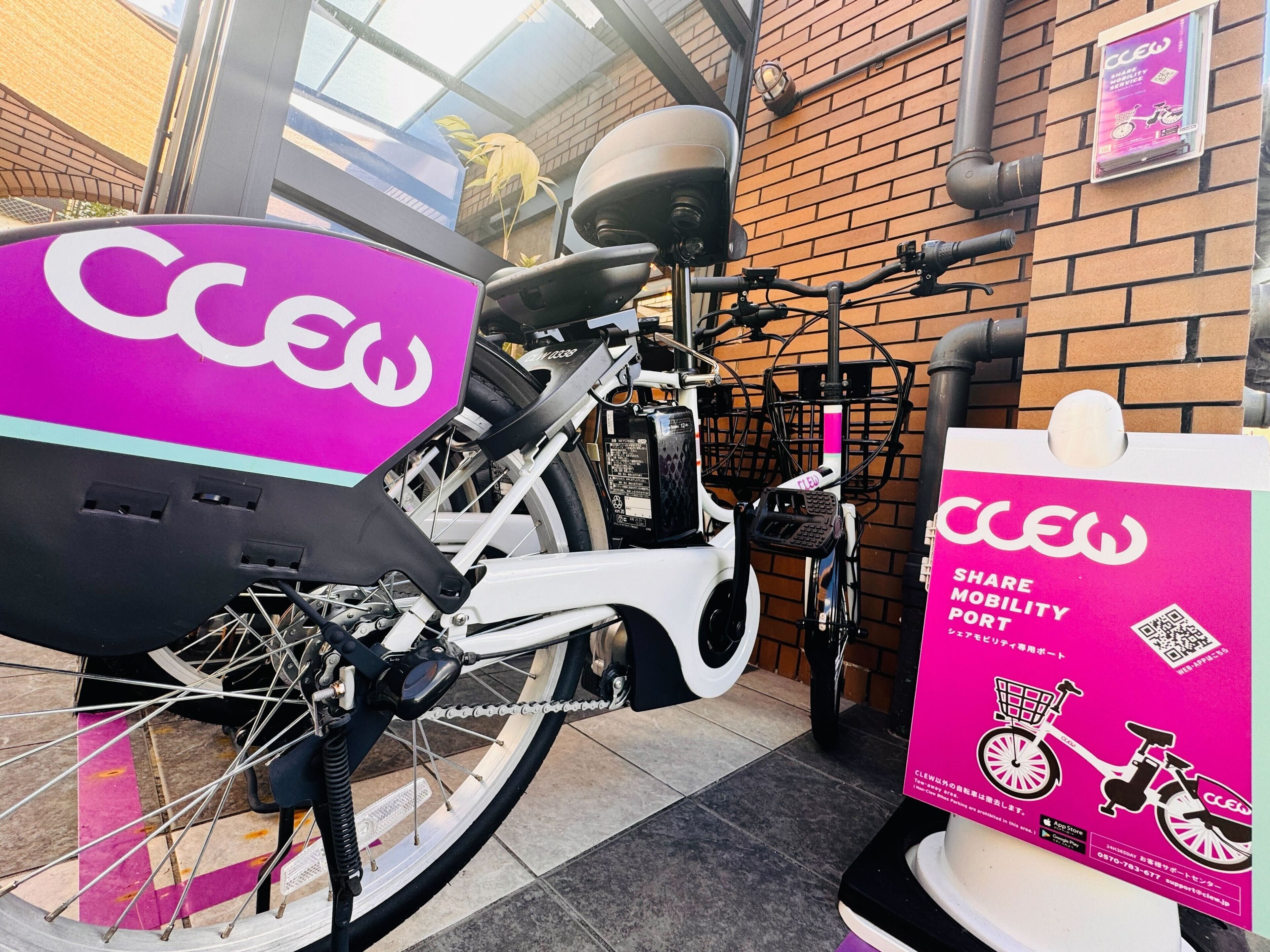 A bicycle with a pink and black color scheme, equipped with a basket and a lock, parked next to a brick wall.
