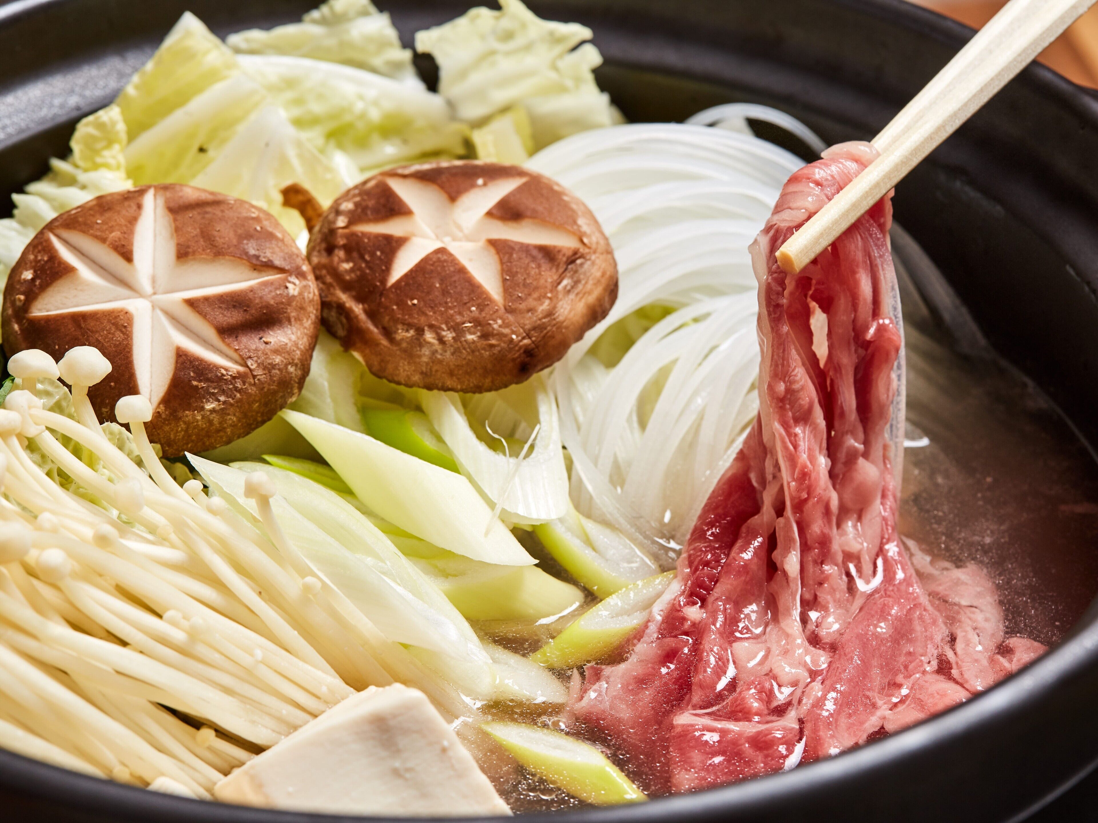 A hot pot with various ingredients including mushrooms, meat, and vegetables.