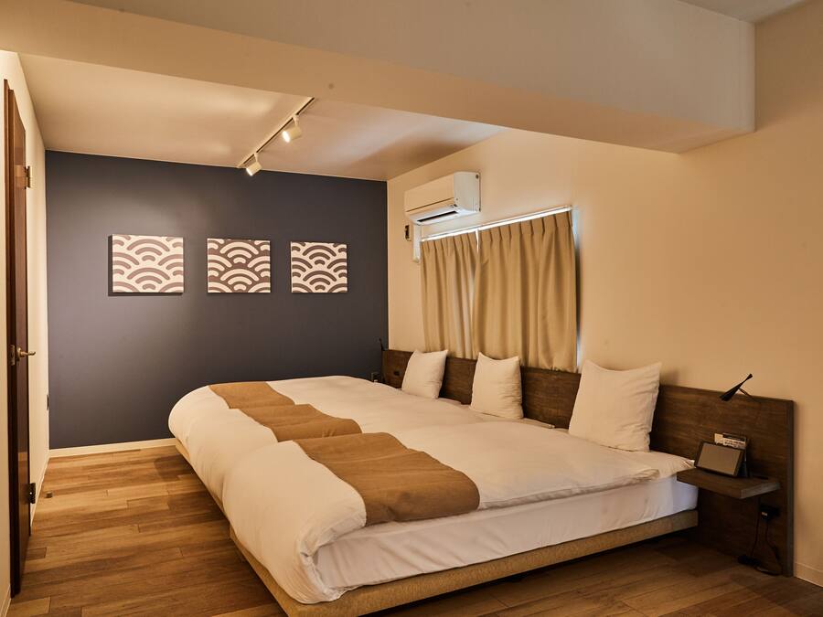 A bedroom with a large bed, a bedside table, an air conditioning unit, and a wall-mounted shelf.