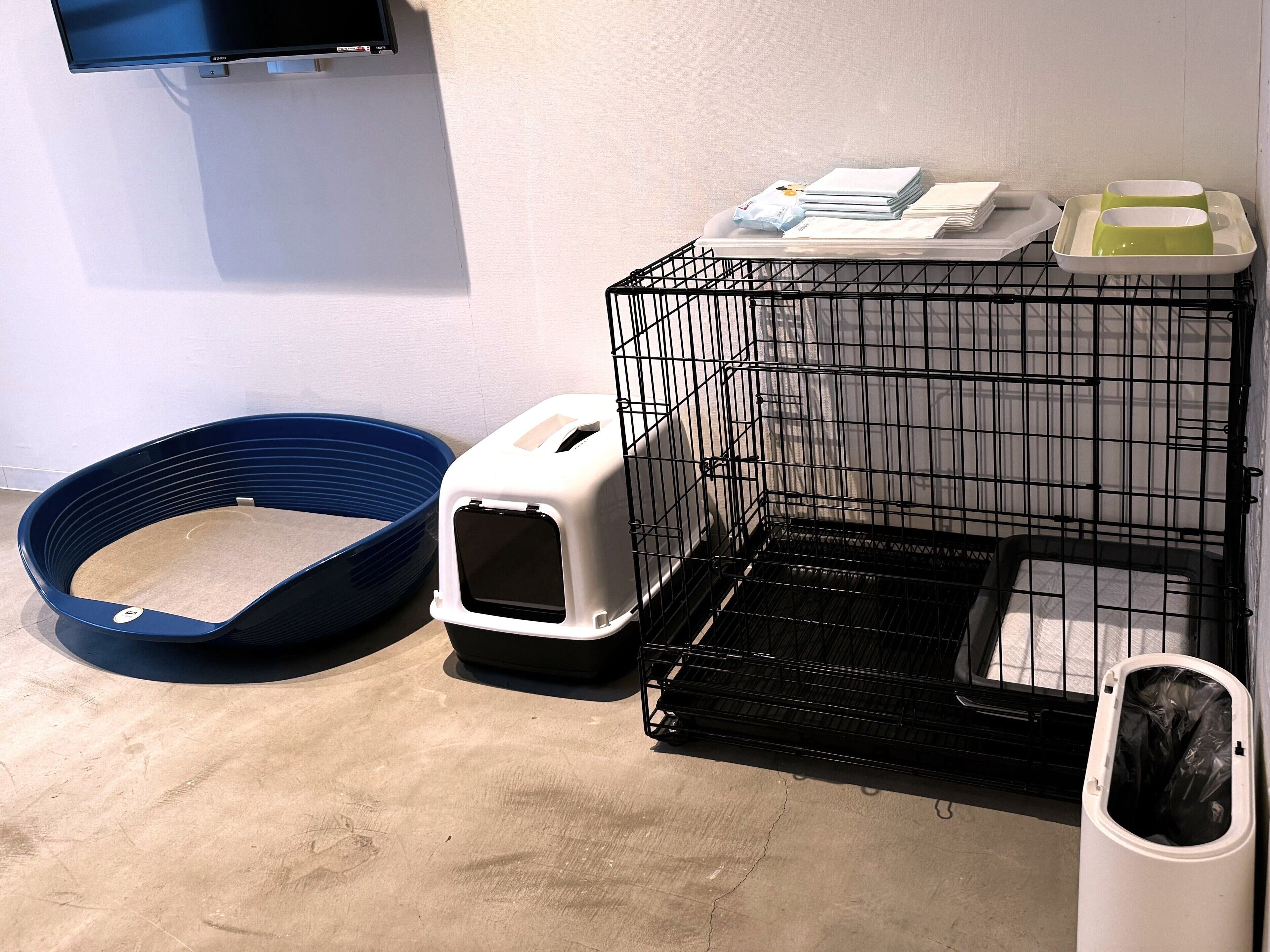 A pet area with a blue pet bed, a white pet carrier, a black pet cage, and a white trash bin.
