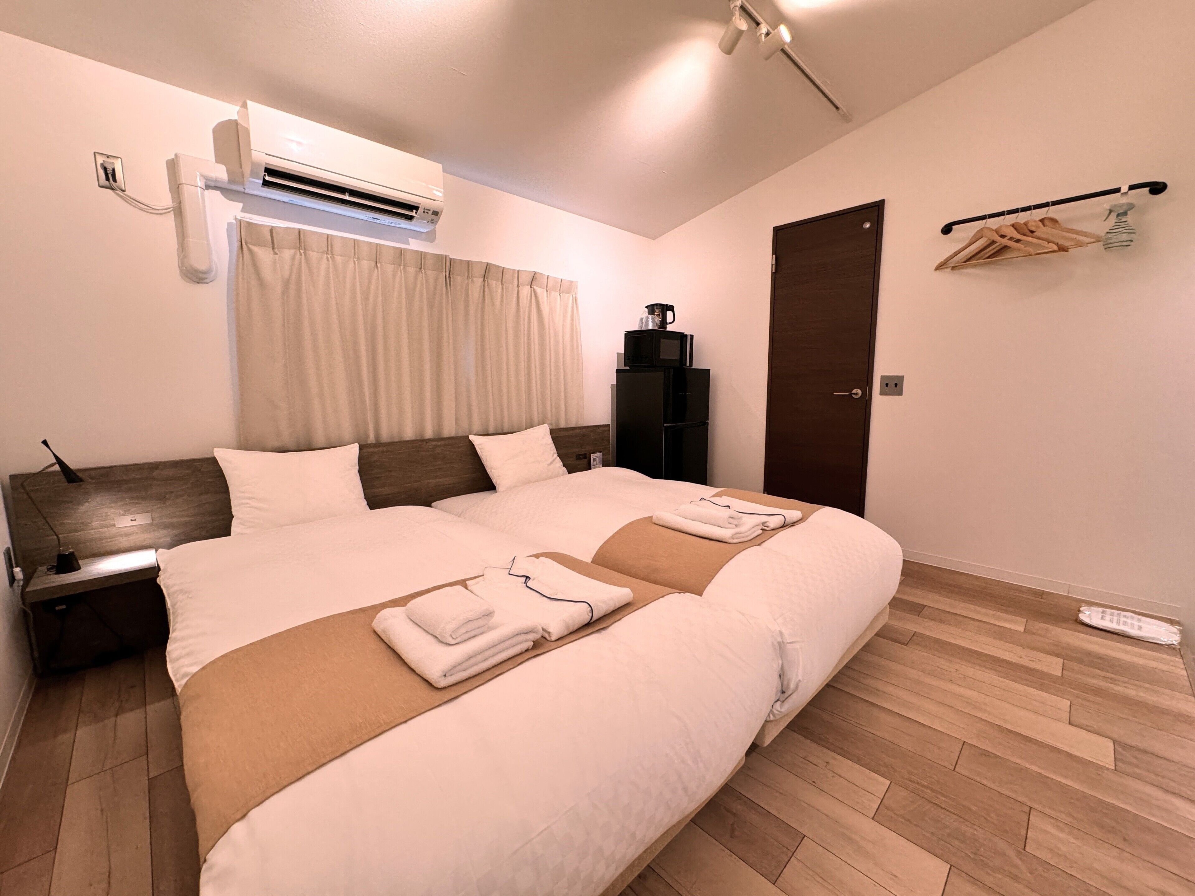 A modern hotel room with a large bed, a built-in air conditioner, a wooden floor, and a dark-colored wardrobe.