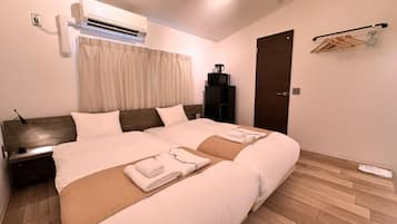A modern hotel room with a large bed, a built-in air conditioner, a wooden floor, and a dark-colored wardrobe.