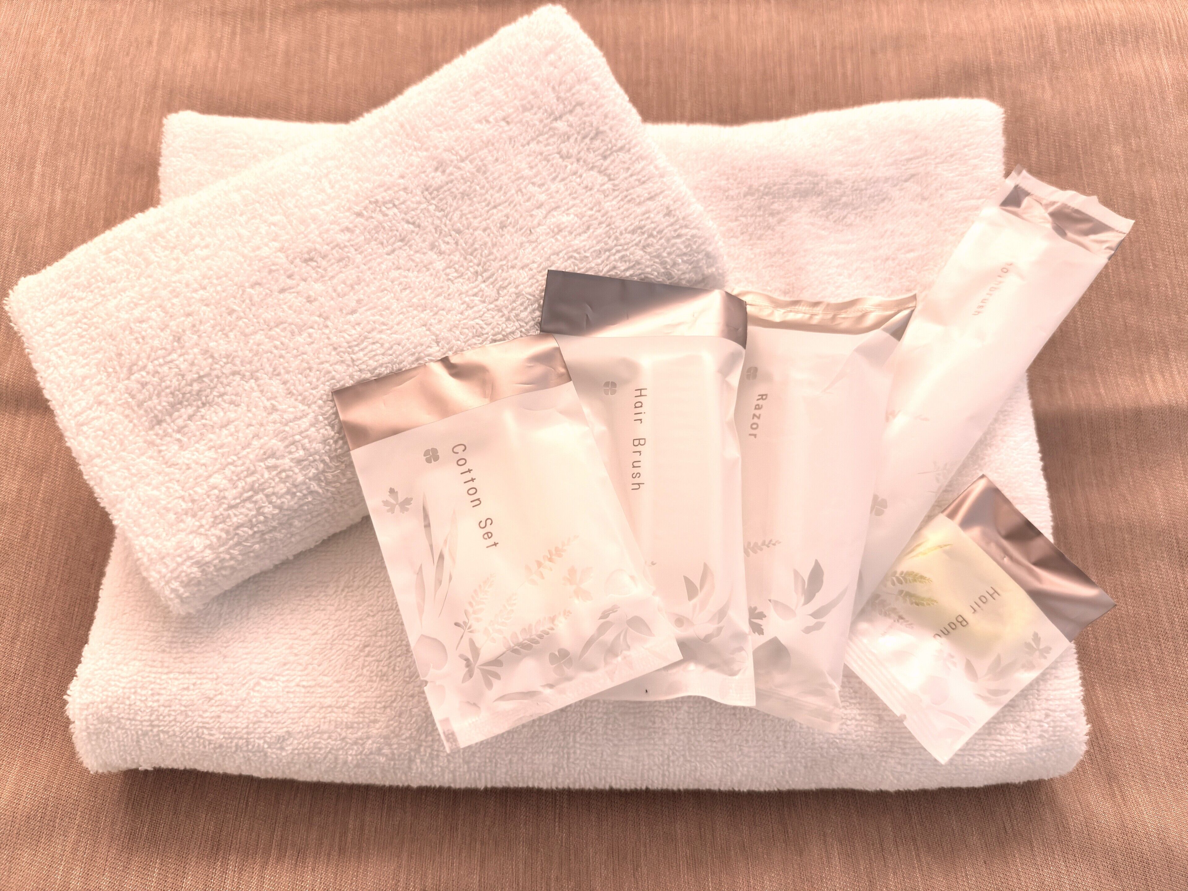 A neatly folded white towel and several toiletry bags labeled "Hair Brush," "Cotton Set," and "Razor."