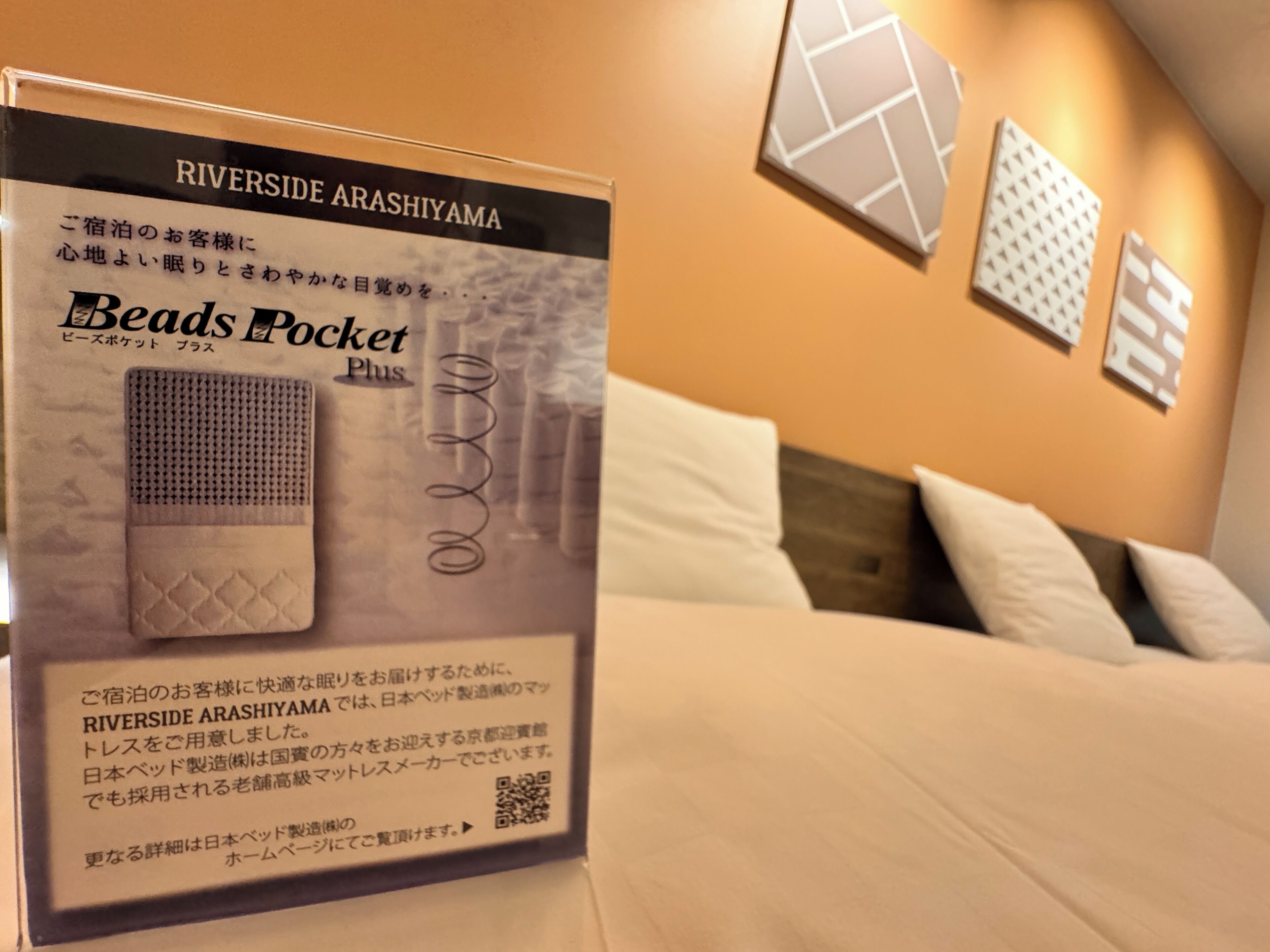A sign for Beads Pocket Plus in a hotel room with a bed and pillows, and decorative wall panels.