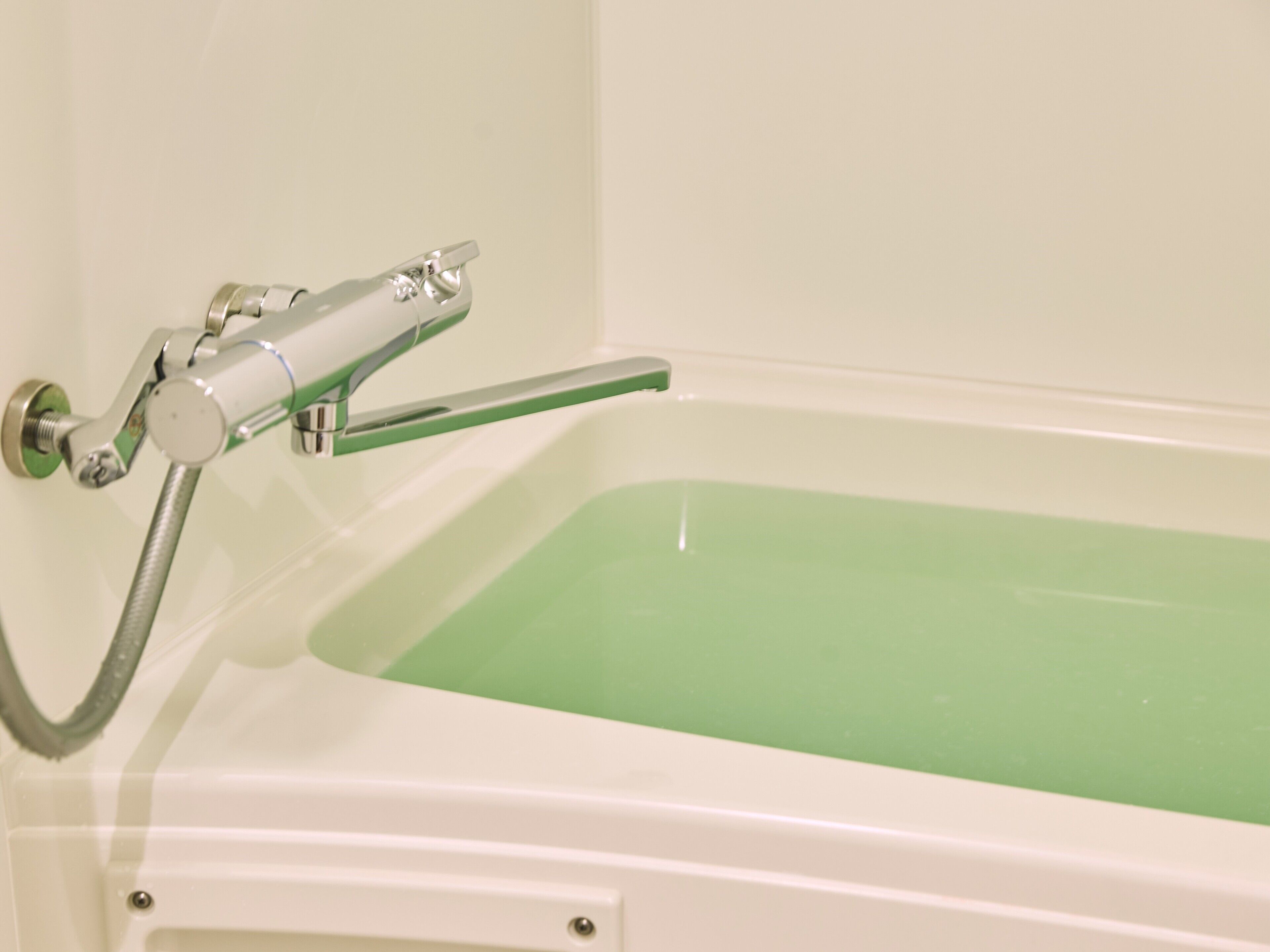 Une baignoire avec un intérieur vert, un robinet chromé et une pomme de douche.