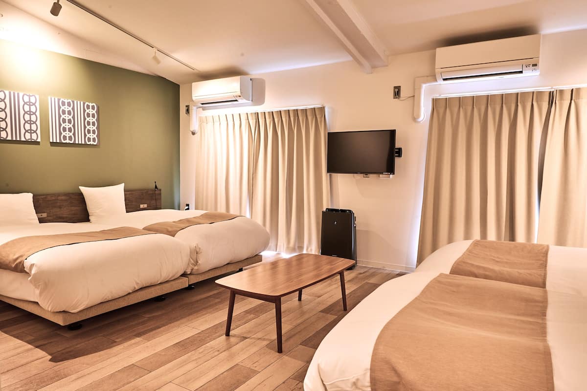 A hotel room with two beds, a flat-screen TV, an air conditioning unit, and a wooden coffee table.