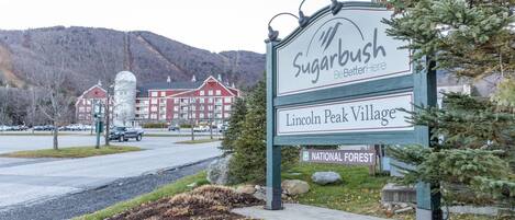 Un panneau indiquant l’entrée du complexe Lincoln Peak Village, avec en arrière-plan un bâtiment et des montagnes.