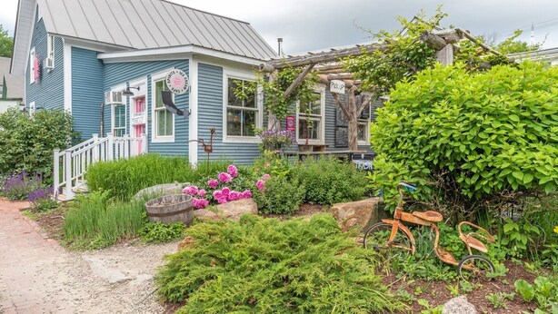 A quaint house with a porch, surrounded by lush greenery and a garden. - 41 Summit Condo Near Mountain Shuttle by RedAwning (Warren)