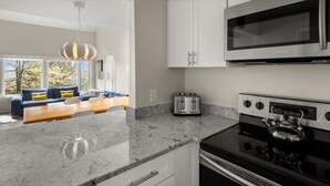 A modern kitchen with a built-in microwave, toaster, and stove. There is a seating area with a sofa and a dining table. - 41 Summit Condo Near Mountain Shuttle by RedAwning (Warren)