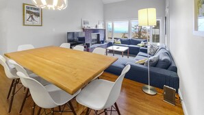 A modern living room with a wooden dining table, white chairs, a blue sofa, and a fireplace. - 41 Summit Condo Near Mountain Shuttle by RedAwning (Warren)