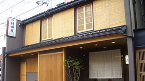 Un edificio japonés tradicional con fachada de madera, un acceso cubierto y una planta en maceta.