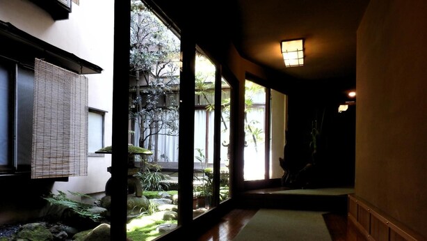 Un pasillo con suelo de madera, un pequeño jardín interior y vistas a un edificio tradicional japonés en el exterior.