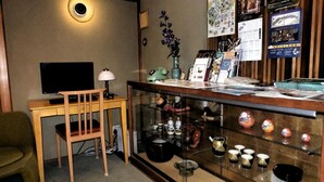 Una habitación con escritorio, silla, televisión, lámpara, objetos decorativos y una vitrina de vidrio con cerámicas.