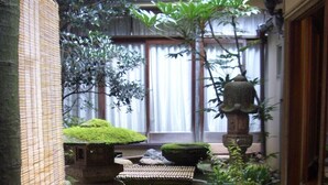 Un jardín japonés tradicional con un farol de piedra, rocas cubiertas de musgo y plantas en macetas.