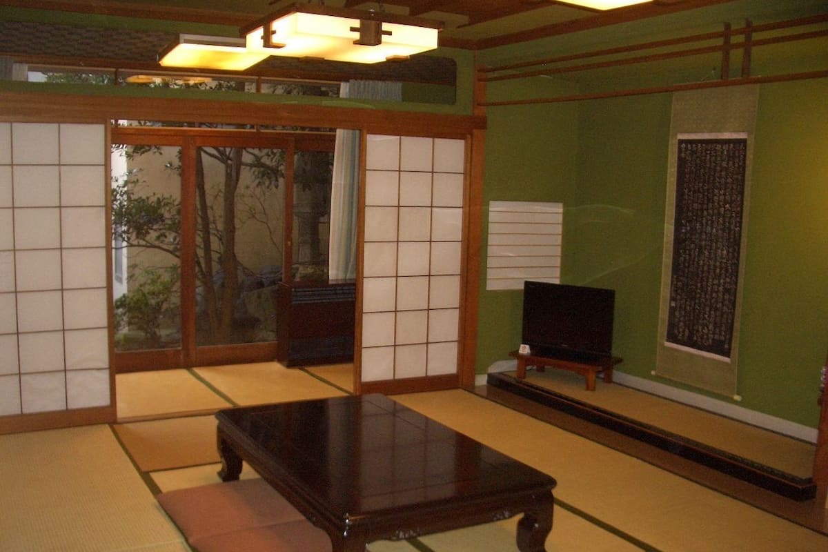 Um quarto japonês tradicional com tatame, uma mesa de madeira baixa, portas deslizantes e uma televisão.