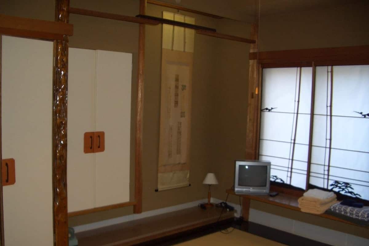 Quarto japonês tradicional com tatames, uma porta deslizante, uma televisão e uma janela com vista para bambus.
