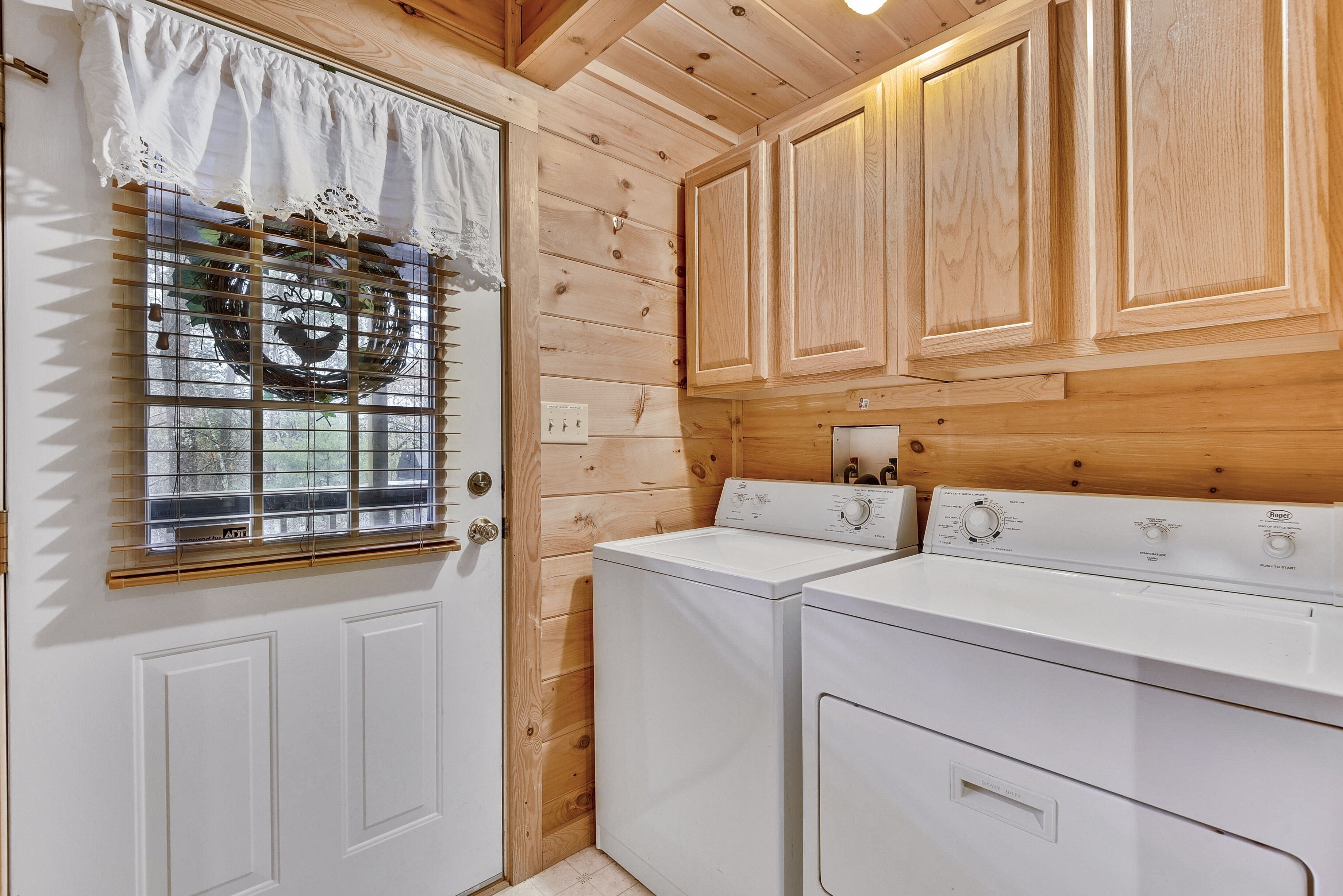 A laundry room with wooden walls, a white door, and two white washing machines.
