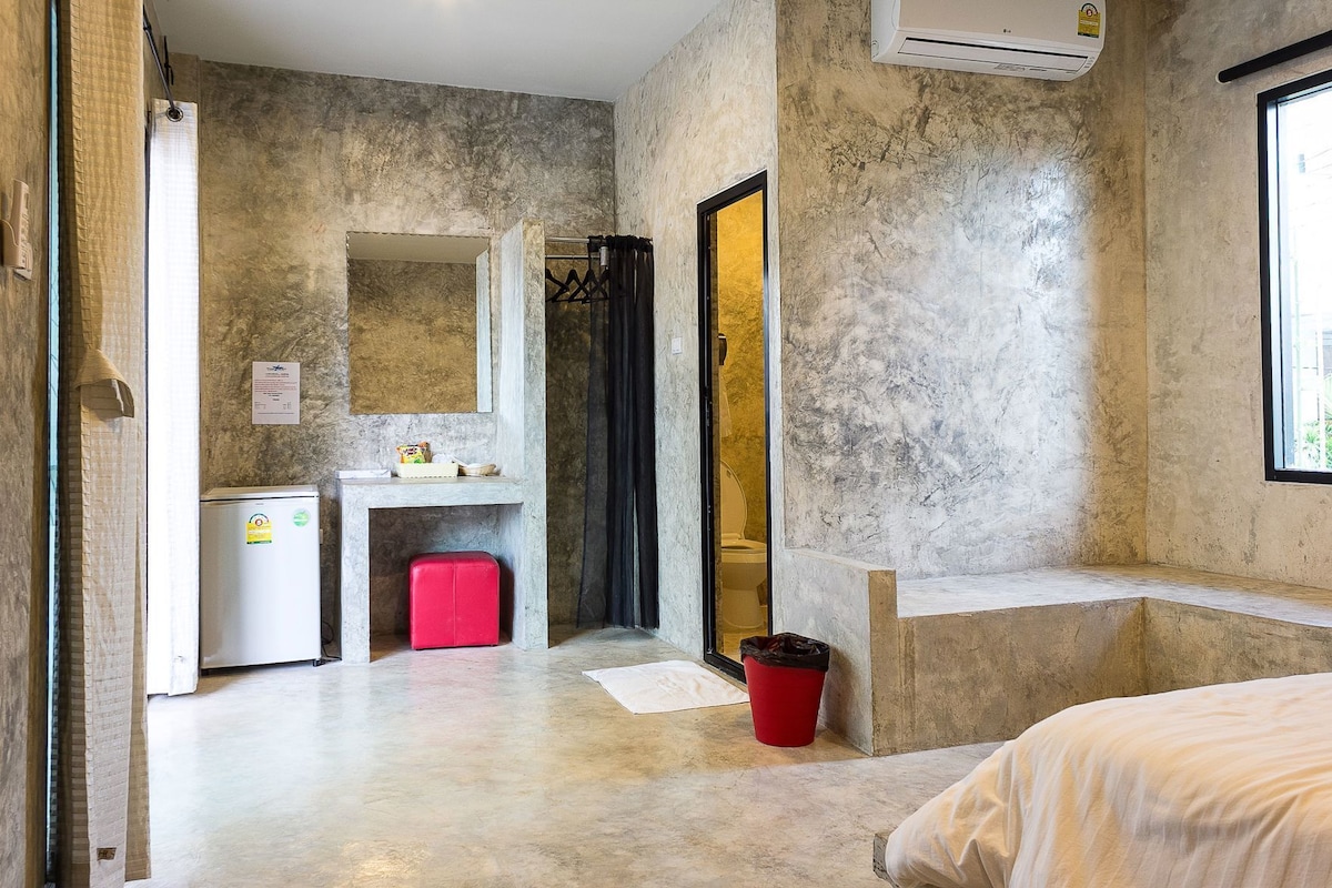 A hotel room with a bathroom, a small kitchenette, a red stool, and a window.
