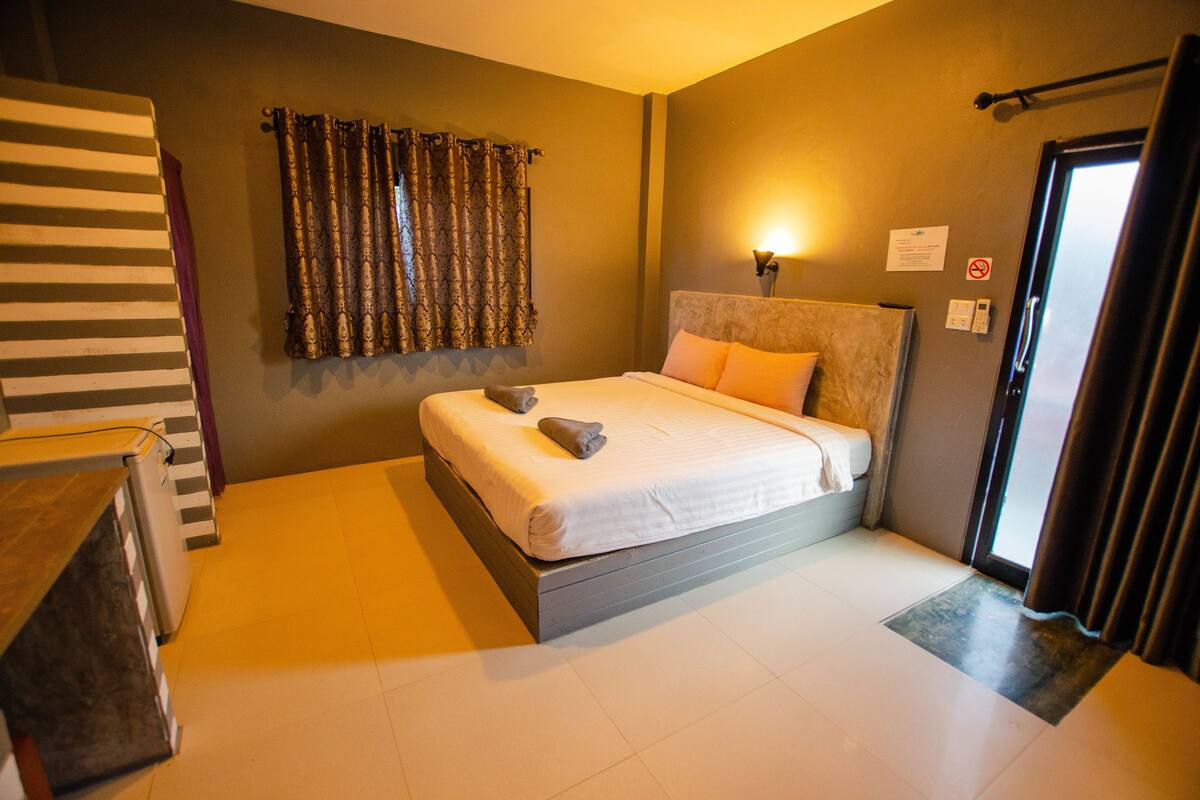 Quarto de hotel moderno com uma cama grande, mesa de cabeceira, guarda-roupa e uma janela com cortinas.