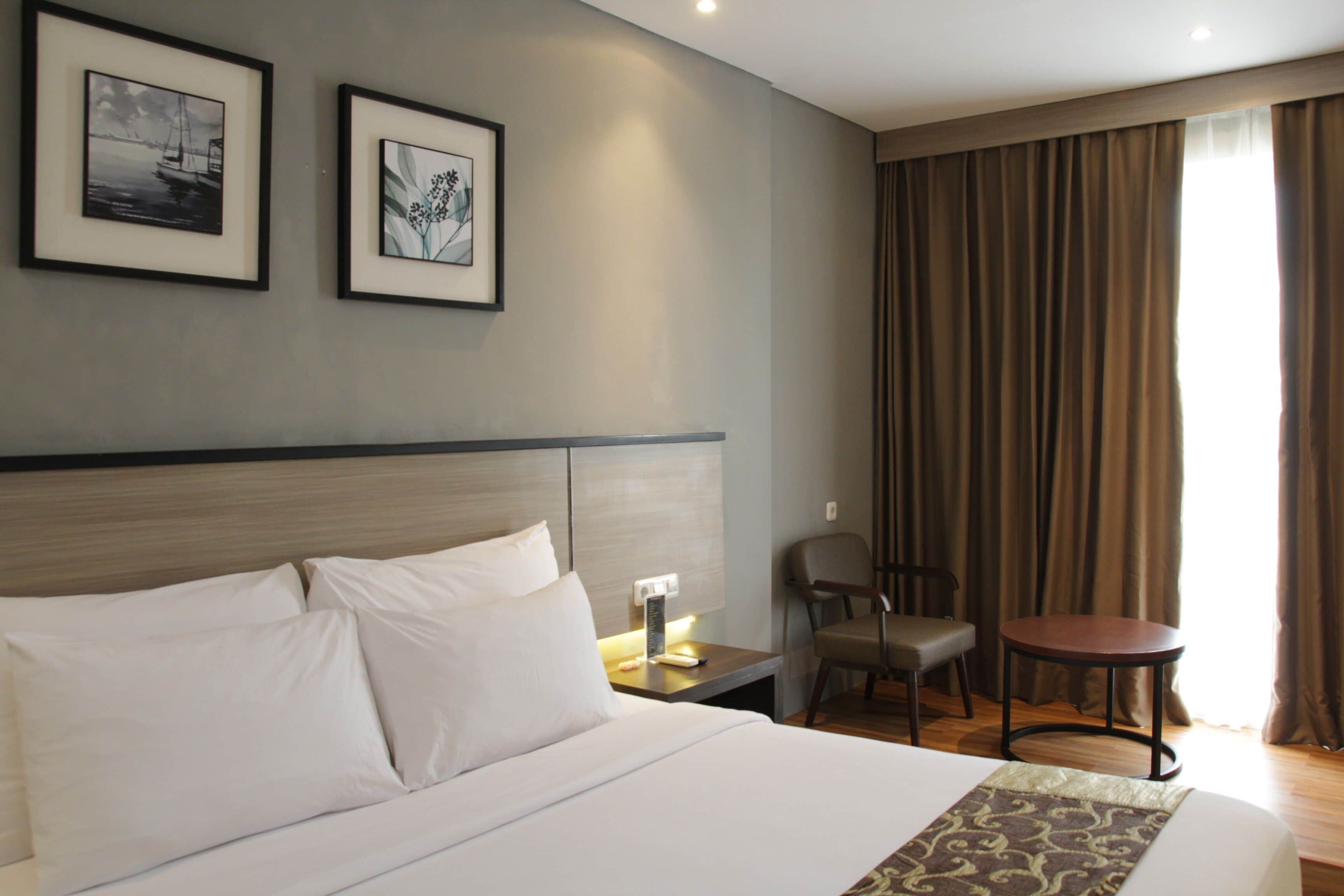 Habitación de hotel con una cama grande, una mesita de noche, una silla, una pequeña mesa y dos cuadros en la pared.