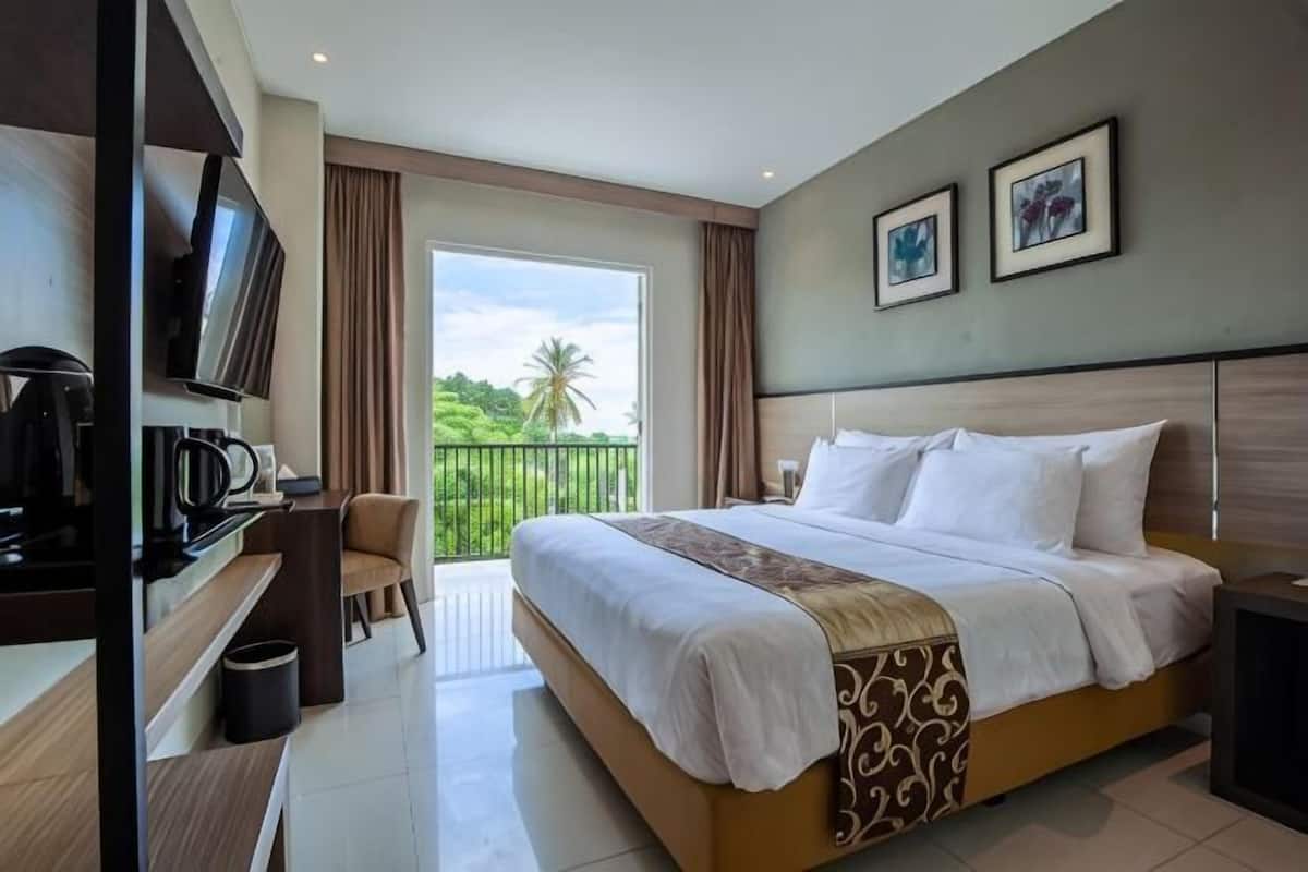 Ein Hotelzimmer mit Bett, Schreibtisch mit Fernseher, Stuhl und Balkon mit Blick auf Grünflächen.