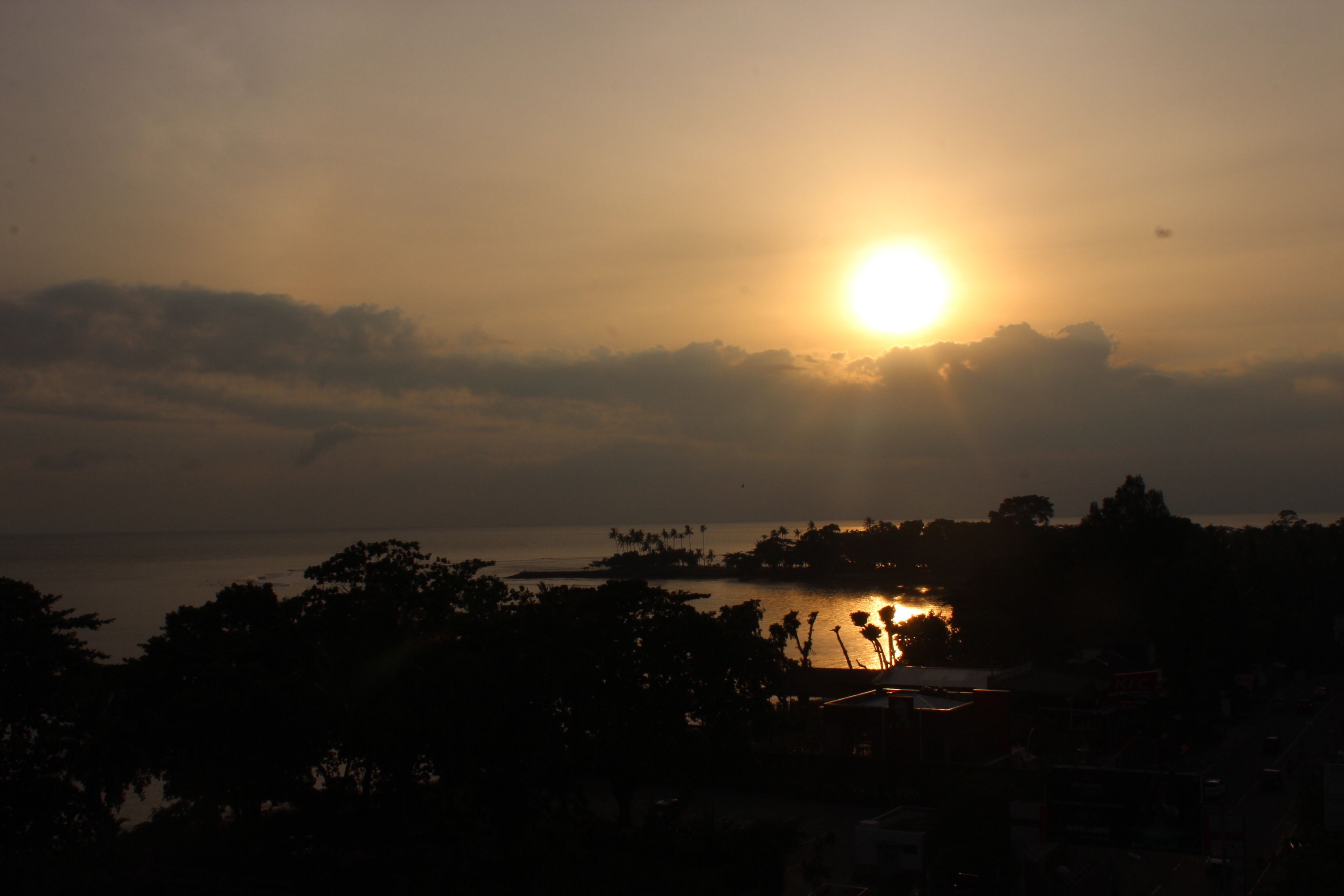 A sunset over a body of water with silhouettes of trees and buildings.