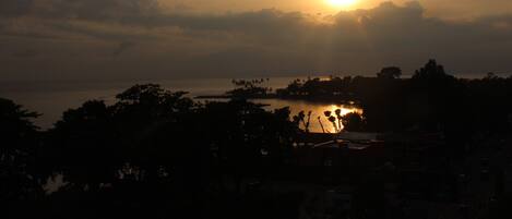 A sunset over a body of water with silhouettes of trees and buildings.