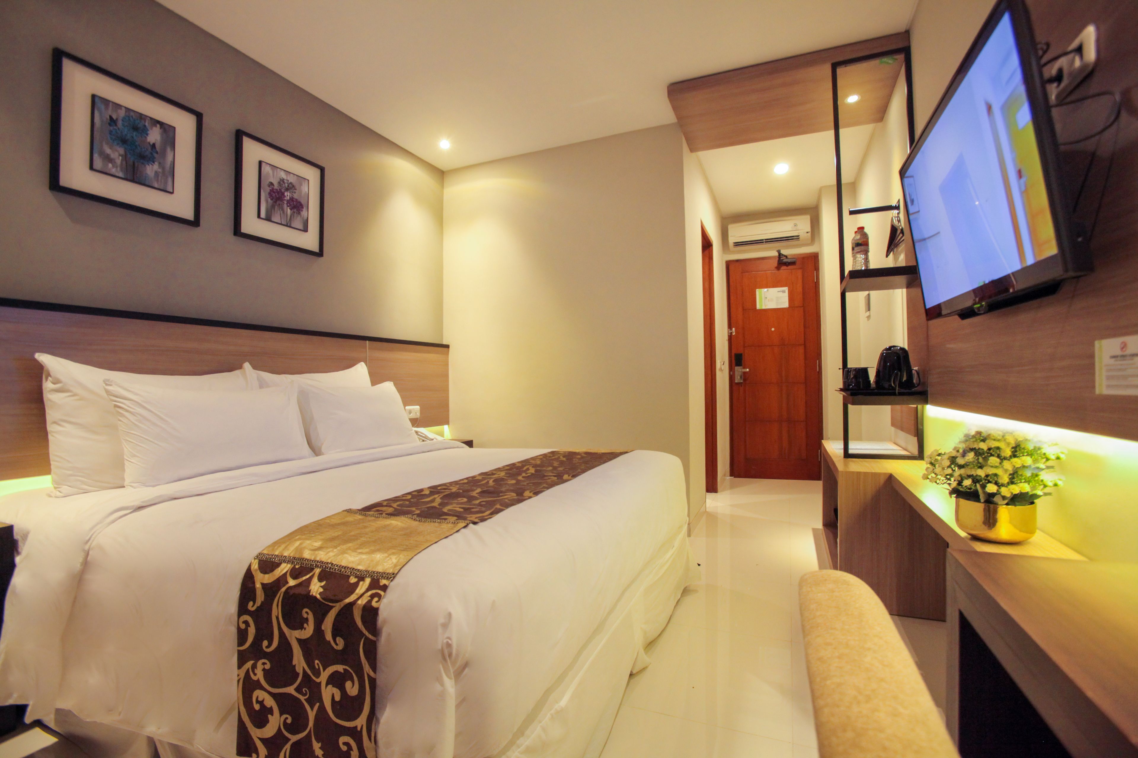 A hotel room with a large bed, a desk with a computer, and a TV mounted on the wall.