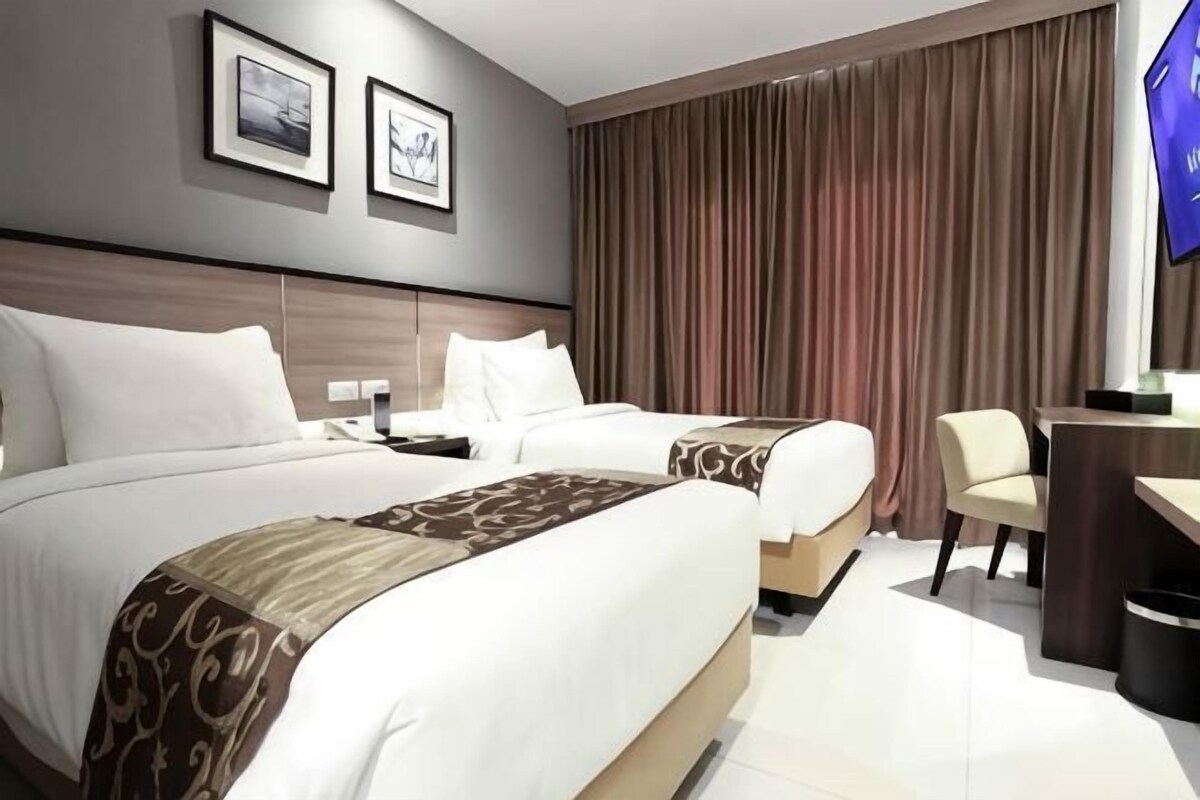 A hotel room with two beds, a desk, a chair, a TV, and a large window with curtains.