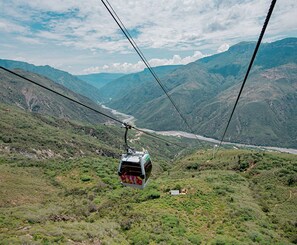 A cable car moving over a mountainous landscape with a river below. - Hostel Santander Aleman Terrace Vista (San Gil)