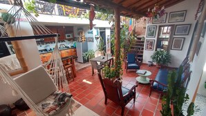 Uma sala de estar aconchegante, com uma rede, móveis de madeira e uma cozinha ao fundo.