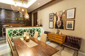 A modern dining area with a wooden table, cushioned chairs, a wooden bench, and a bar area with a stone wall backdrop.