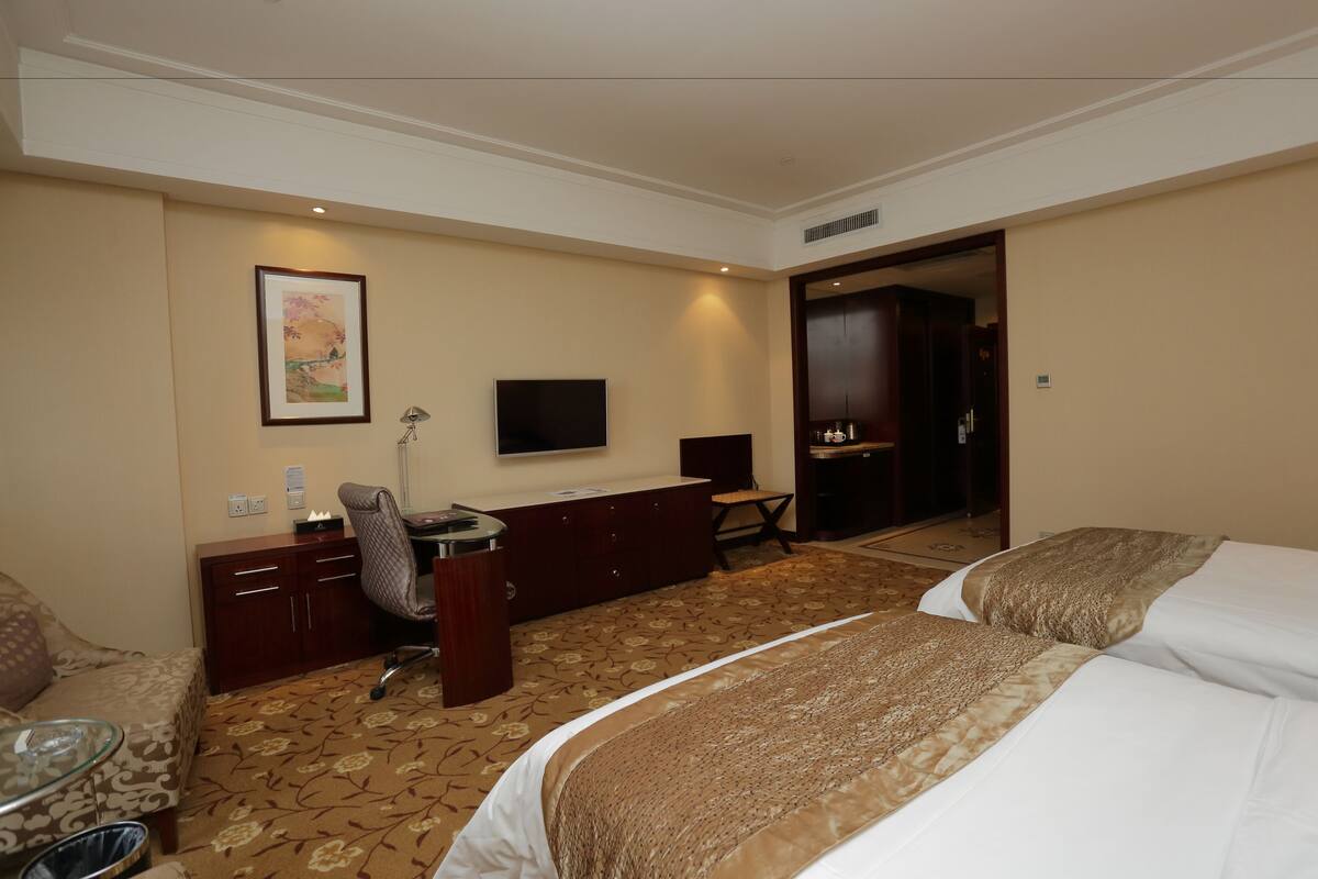 Une chambre d’hôtel équipée d’un lit, d’un bureau, d’une chaise, d’une télévision et d’une porte donnant sur une autre pièce.