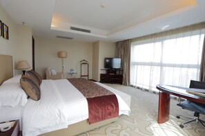 A hotel room with a large bed, a desk with a chair, a television, and a window with curtains. - Arcadia International Hotel (Langfang)