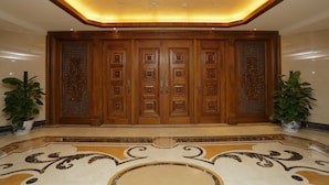 A grand entrance with a large wooden door, a decorative floor, and two potted plants. - Arcadia International Hotel (Langfang)
