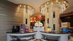A hotel reception area with two curved counters, a coffee machine, a fruit display, and decorative hanging lights. - Arcadia International Hotel (Langfang)