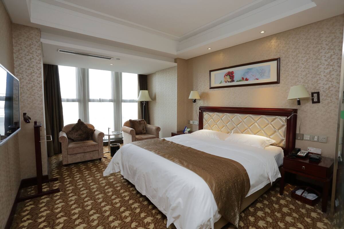 Une chambre d’hôtel avec un grand lit, deux fauteuils, une télévision et un tableau au mur.