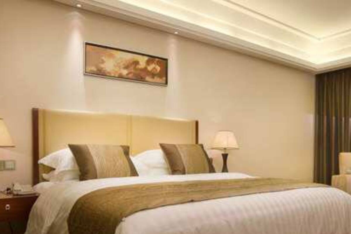 Une chambre d’hôtel avec un grand lit, deux tables de chevet, une commode, un tableau au mur et une fenêtre avec des rideaux.