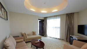 A modern hotel room with a sofa, armchair, and a small table. There is a TV on the wall and a window with curtains. - Arcadia International Hotel (Langfang)